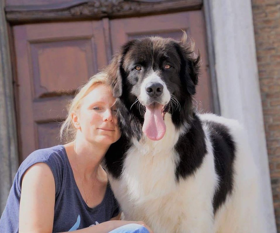 Porträt von Apothekerin Jennifer Stock im Freien, gemeinsam mit einem großen schwarz-weißen Hund. Beide blicken in die Kamera, im Hintergrund ist ein Gebäude zu sehen.